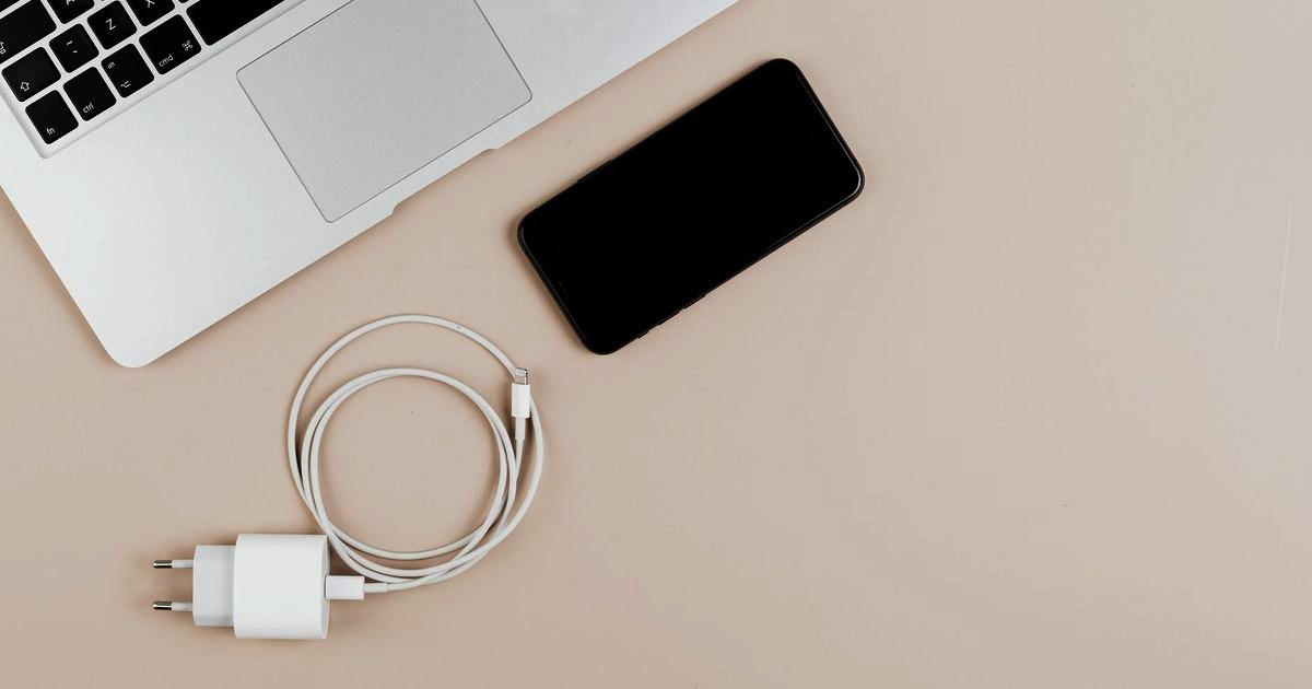 A white charger block, coiled cable and phone on a cream desk