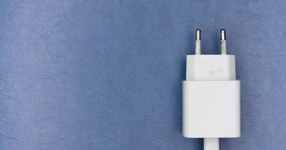 White USB-C charger block with its cable on a textured blue background
