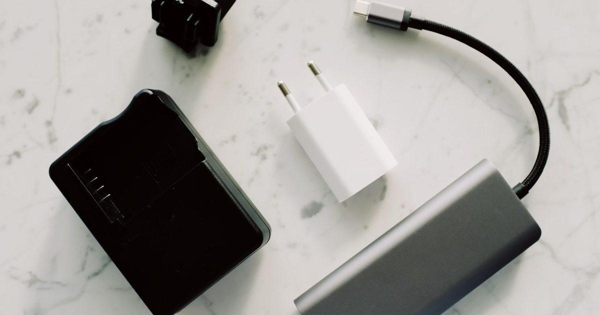 Black laptop charger, white charger block and a braided USB-C cable on marble