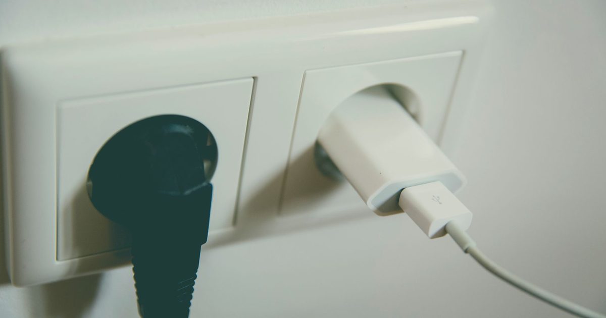 White USB charger plugged into a wall socket next to a black plug