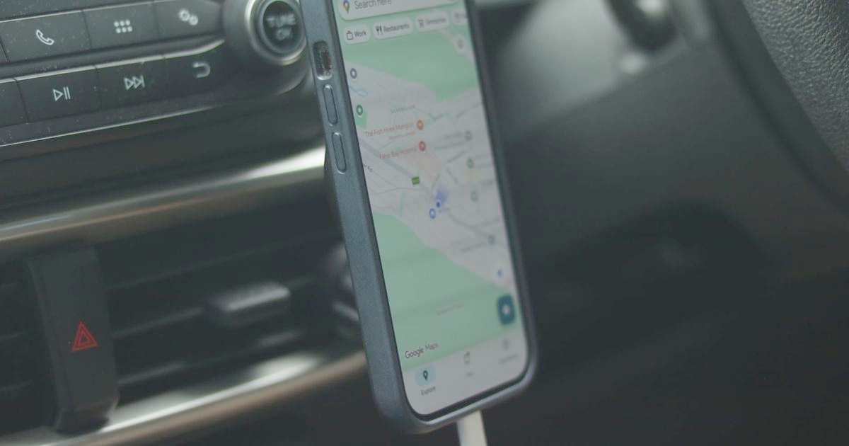 A phone showing a map in a car vent mount with a cable