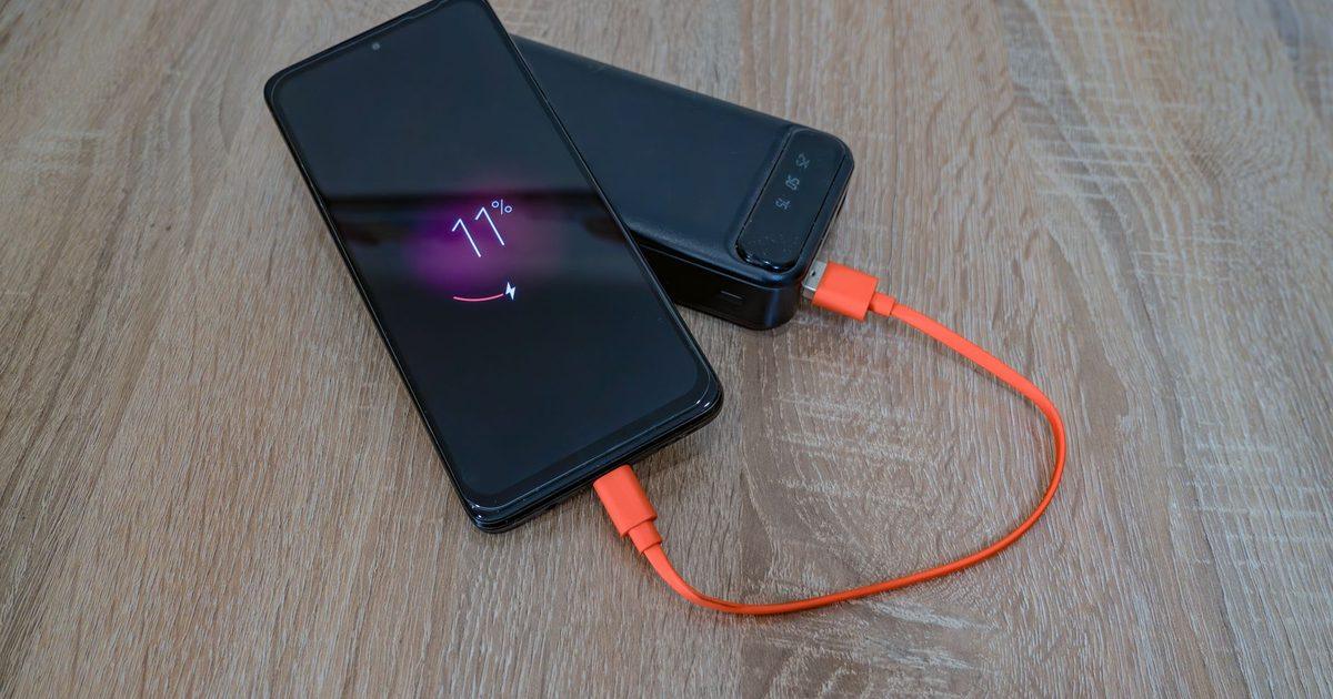 A phone charging from a power bank by an orange cable on wood