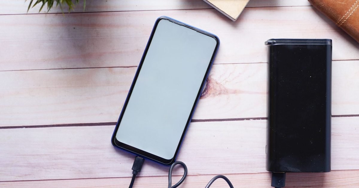 A phone and a black power bank with cables on a wooden table