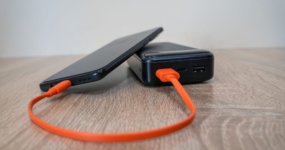 A phone charging from a power bank through an orange USB-C cable
