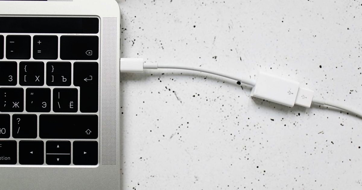 A white USB-C cable plugged into a laptop on a white desk
