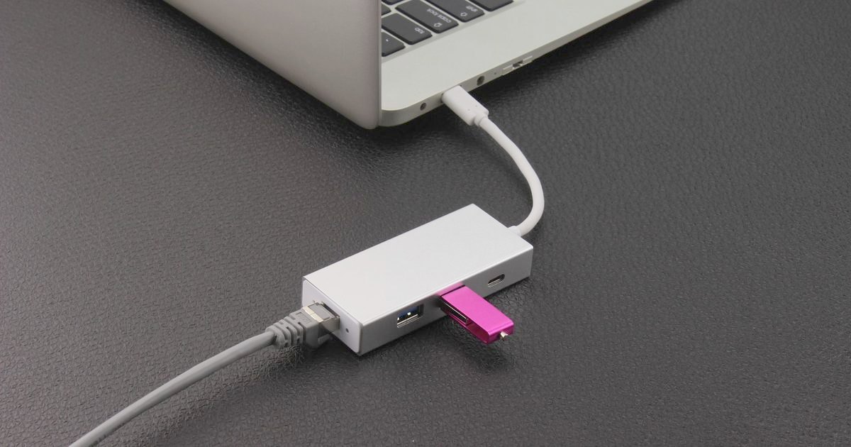 A white USB hub with an ethernet cable plugged in beside a laptop