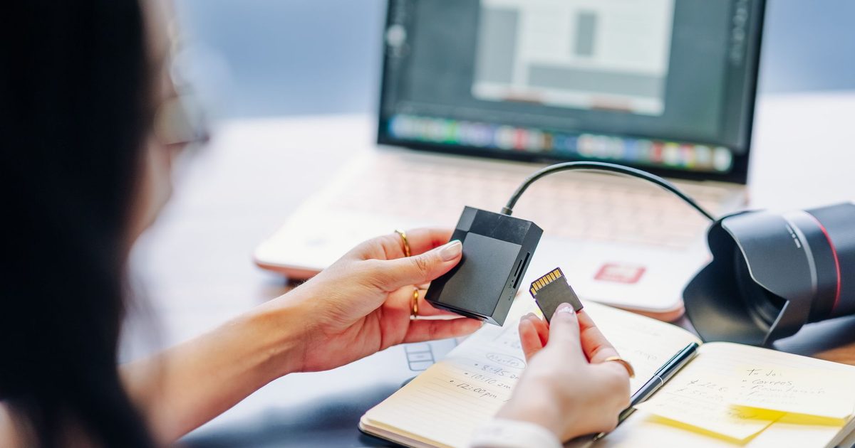 A hand sliding an SD card into a reader attached to a laptop