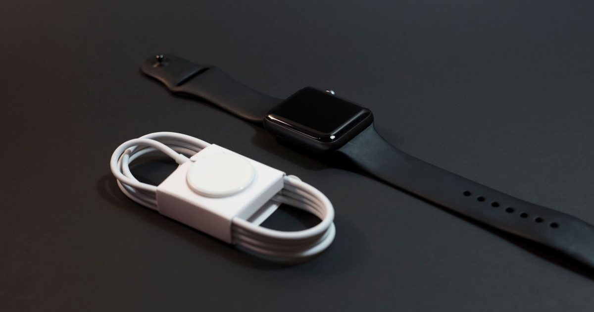 a smartwatch beside its round magnetic charging puck and coiled white cable