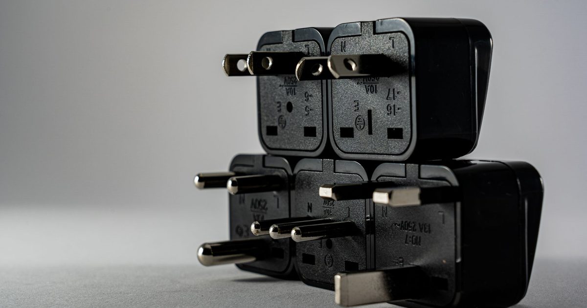 a stack of black universal travel plug adapters with assorted international prongs