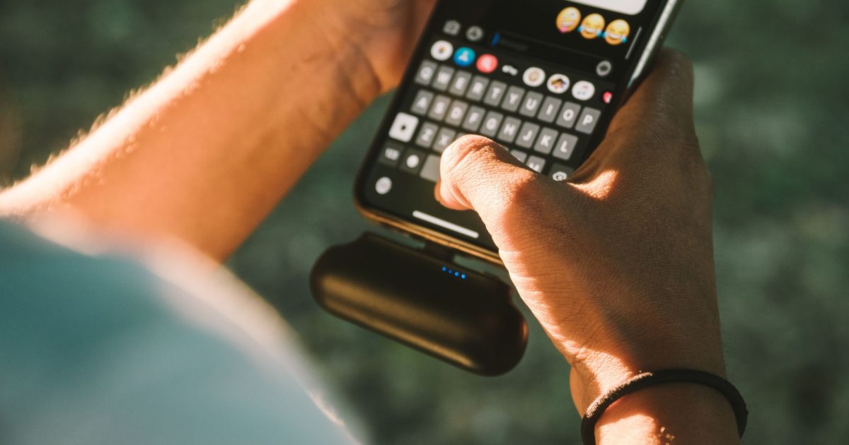a hand holding a phone charged by a small power bank outdoors
