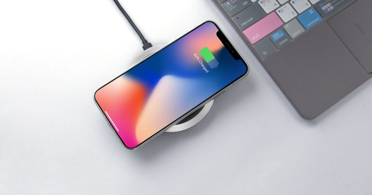 a smartphone charging on a round wireless pad beside a laptop