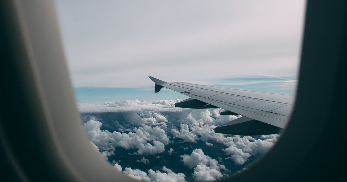 View from an airplane window seat of the wing above a layer of cloud