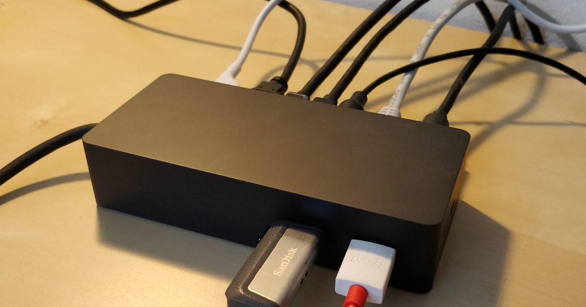 A black docking station on a desk with cables plugged into its ports