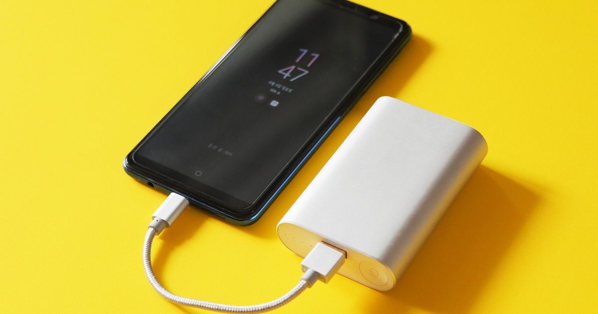 a power bank charging a phone with a short cable on a yellow background